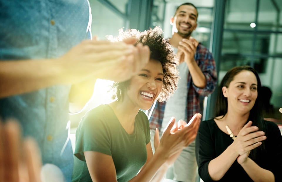 Un groupe de jeunes gens sourient et applaudissent dans un bureau