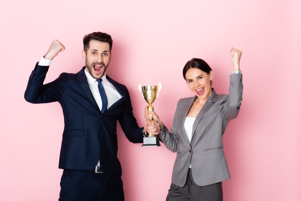 Un homme et une femme devant un fon rose qui porte un trophée en souriant